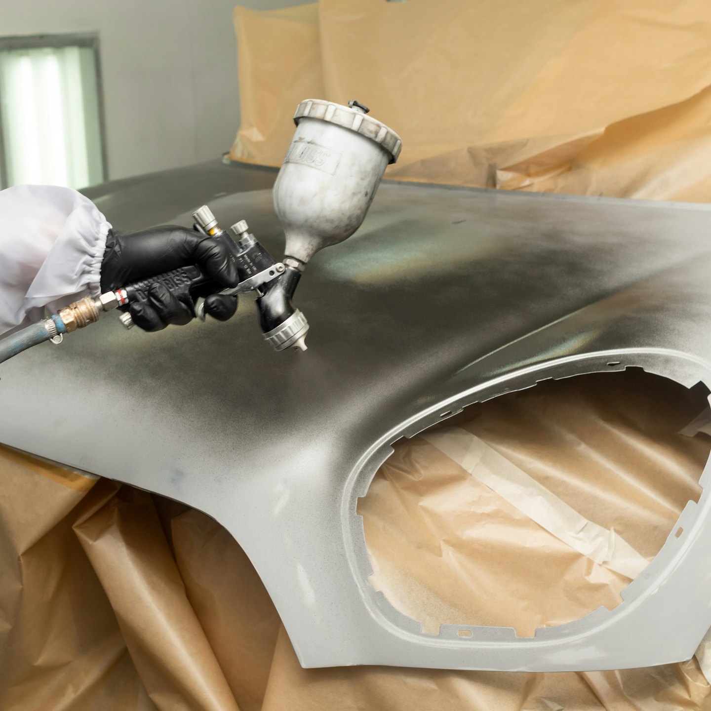 A technician sprays grey primer onto a masked car fender.