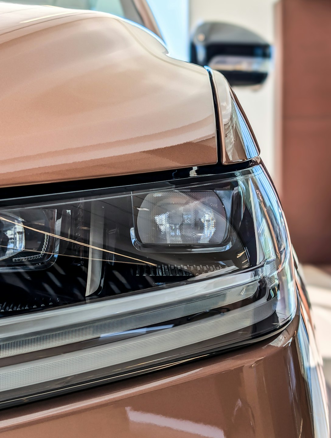 The sleek headlight and metallic copper hood of a car.